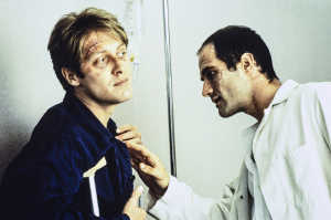 James Ballard (James Spader) dejndose examinar por Vaughan (Elias Koteas) extadiado con las heridas de su cuerpo